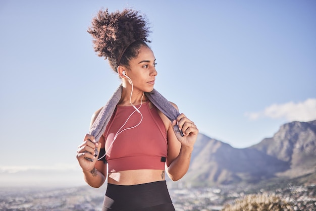 Toalla de fitness y mujer negra con auriculares en la naturaleza después de hacer ejercicio o entrenar Bienestar de la salud o transmisión de música femenina radio o audio de podcast o canción en un descanso después de hacer ejercicio solo
