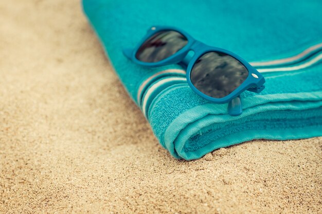 Foto toalla y gafas de sol en la playa de arena