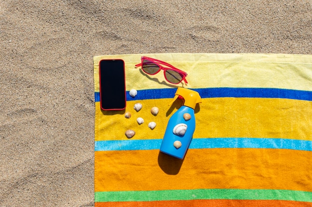 Foto toalla protector solar gafas de sol y teléfono inteligente en la playa concepto de verano