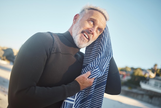 Toalla de surfista y nadar con un anciano secando el cabello después de nadar, surfear y practicar deportes acuáticos durante una aventura de viaje de surf y vacaciones de verano Hombre feliz sonriendo en un traje de neopreno mientras está de vacaciones