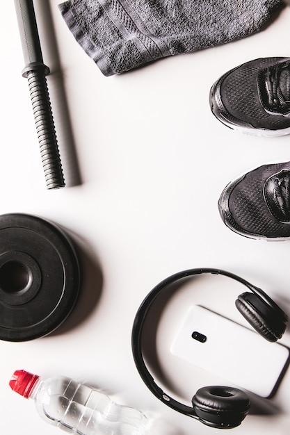 Toalla, zapatillas, agua y smartphone con auriculares sobre un fondo blanco.