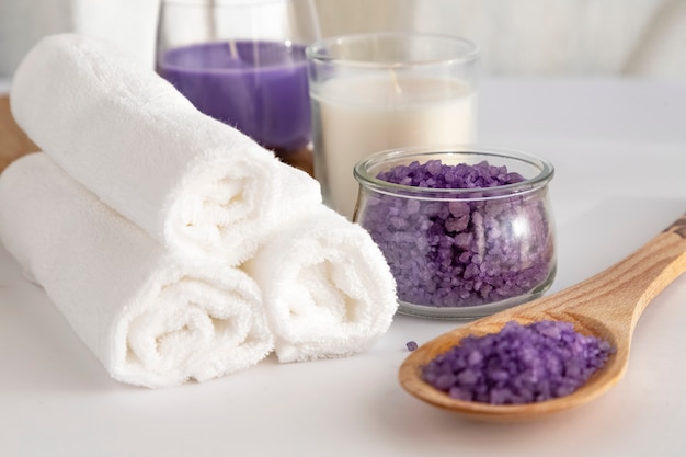 Toallas blancas dobladas en un rodillo sobre un fondo blanco, una vela blanca y lila, sal para los colores del matorral y el olor a lavanda. Concepto de spa. El concepto de limpieza.