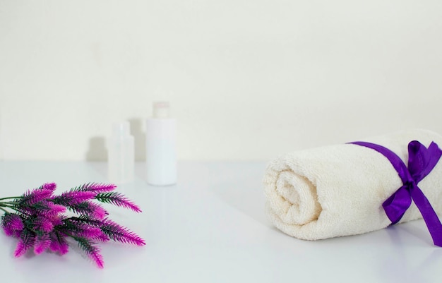 Toallas blancas y una planta de interior sobre una mesa blanca, un lugar para copiar. Una pancarta con cosméticos de lavanda y un lugar para texto. Cuidado de la piel del cuerpo en el hogar, spa.