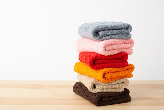 Toallas coloridas frescas dobladas para el baño en la mesa de madera con fondo blanco.