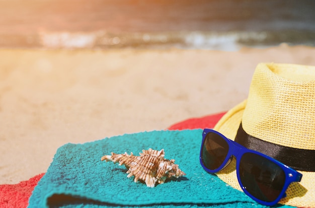 Foto toallas, gafas de sol, concha, sombrero sobre arena en la orilla del mar. vacaciones . el sol brilla brillante.