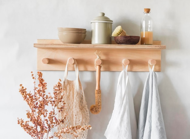 Toallas de lino en un estante de madera con tazones, un frasco de cerámica cepilla flores secas en una habitación luminosa y acogedora de estilo escandinavo