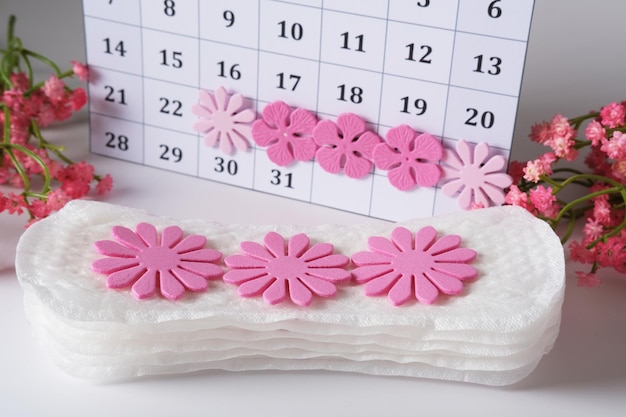 Toallas sanitarias femeninas para el período menstrual decoradas con flores en el fondo del calendario con un ciclo marcado