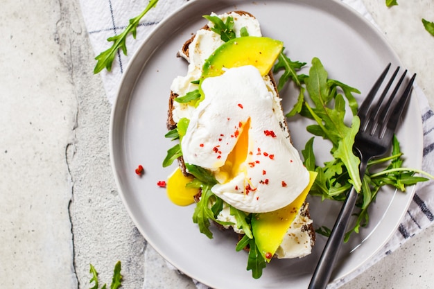 Toast des poschierten Eies mit Avocado-, Frischkäse- und Roggenbrot auf grauer Platte. Gesundes Lebensmittelkonzept.