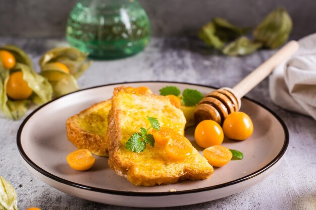 Toast gebraten in Ei mit Physalis-Honig und Minze auf einem Teller Hausgemachtes Dessert