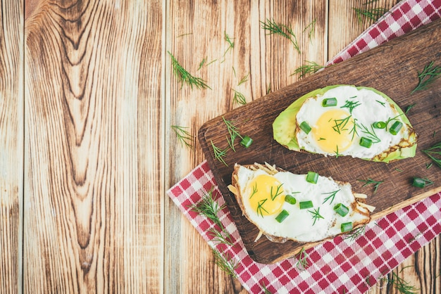Toast mit Avocado, Eiern, Frühlingszwiebeln und Käse auf Holzschneidebrett.