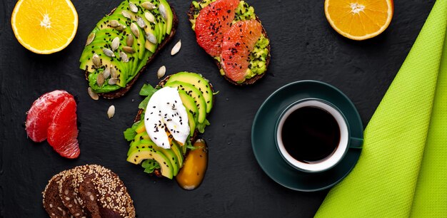 Toast mit Avocado, Sesam, Grapefruit, Orange, Ei und Kaffee auf einem konkreten schwarzen Hintergrund. leckeres Frühstück mit Kaffee und Toast