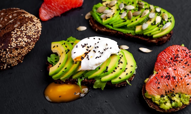 Toast mit Avocado, Sesam, Grapefruit, Orange, Ei und Kaffee auf einem konkreten schwarzen Hintergrund. leckeres Frühstück mit Kaffee und Toast