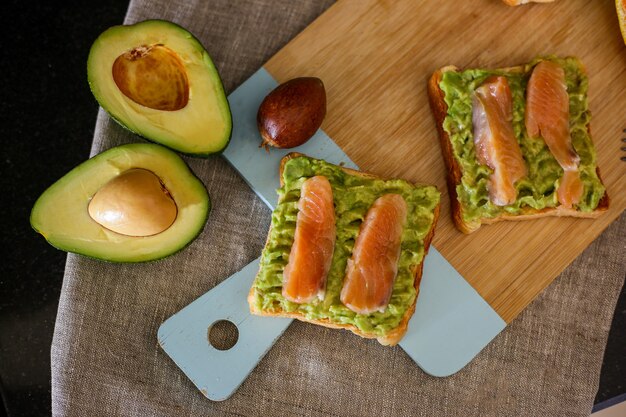 Toast mit Avocado und rotem Sklaven zum Frühstück auf einem Holzbrett, Draufsicht