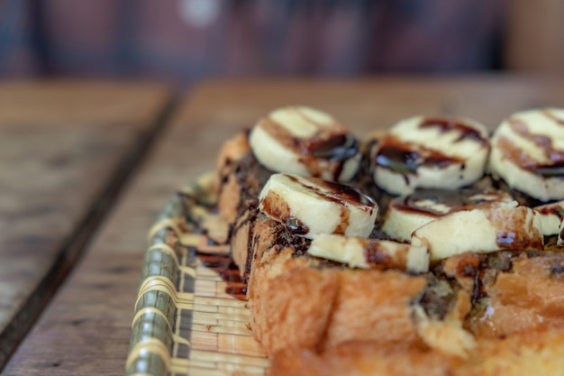 Toast mit Bananen, Schokolade Schocks gekrönt. Holz auf ein klassisches Gericht