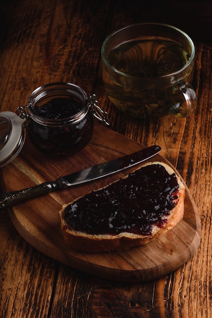Toast mit Beerenmarmelade auf Schneidebrett und Tasse grünem Tee in rustikaler Umgebung