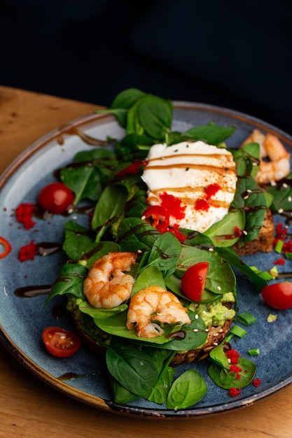 Toast mit Buchweizenbrot, pochiertem Ei, geschnittener Avocado, Garnelen, Tomaten und Salat