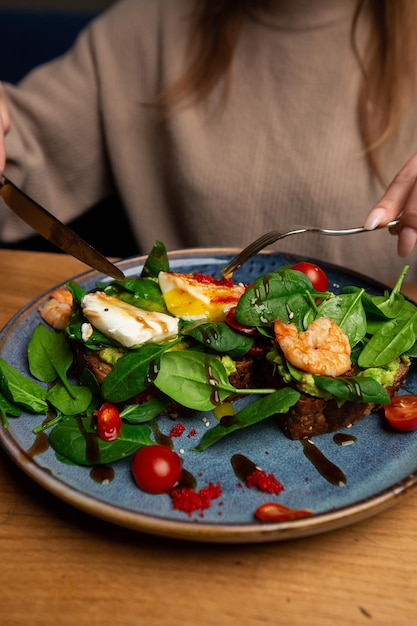 Toast mit Buchweizenbrot, pochiertem Ei, geschnittener Avocado, Garnelen, Tomaten und Salat