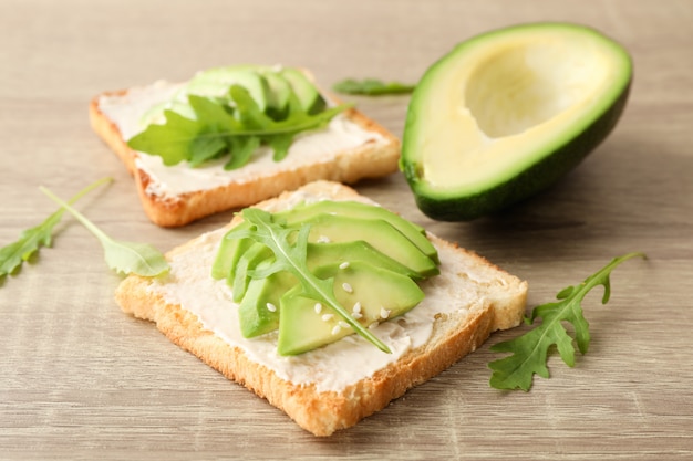 Toast mit Butter, Avocado, Rucola und Sesam auf Holz, Nahaufnahme