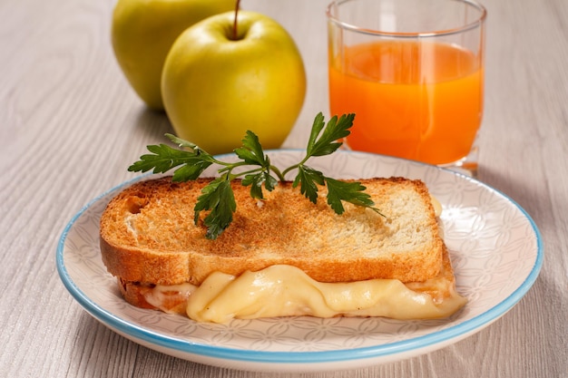 Toast mit Butter und Käse auf weißen Teller zwei Äpfel und ein Glas Orangensaft