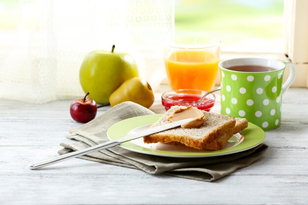 Toast mit Erdnussbutter auf Teller mit Tasse Tee und Saft auf hellem Hintergrund