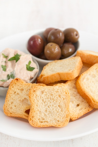 Toast mit Fischpastete und Oliven auf weißem Teller