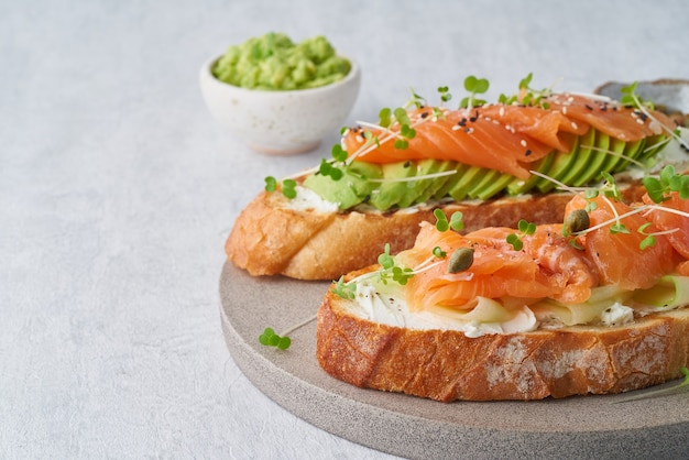 Toast mit Lachs, Frischkäse und Gurkenscheiben auf weißem Betontisch