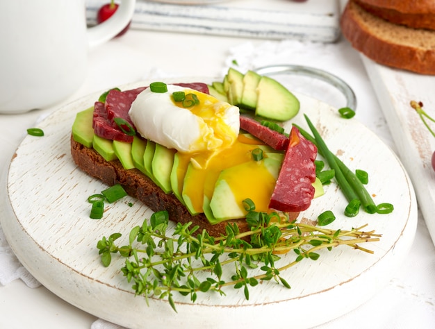 Toast mit pochiertem Ei und Avocado auf einem runden Brett, Frühstück am Morgen