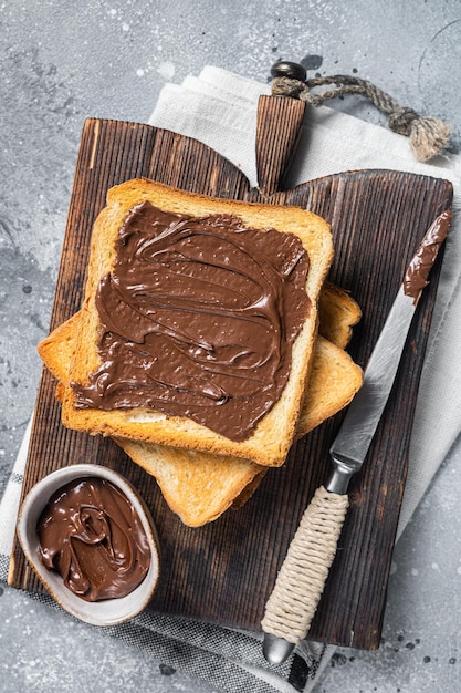 Toast mit Schokoladen-Haselnussaufstrich auf Holzbrett Grauer Hintergrund Ansicht von oben