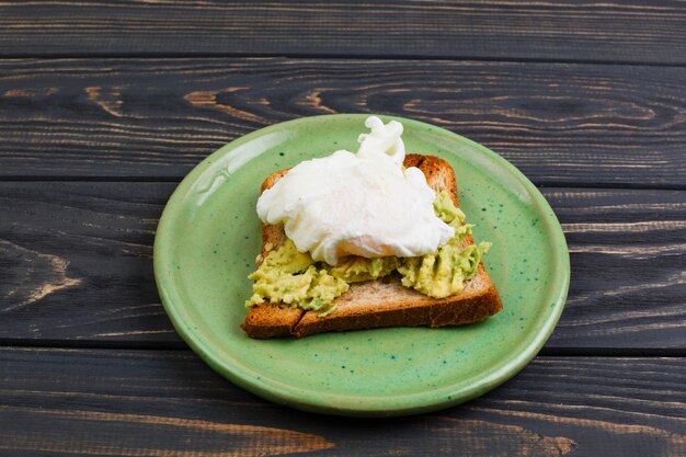 Toast und poschiertes Ei mit Avocado auf einer grünen Platte auf Holztisch