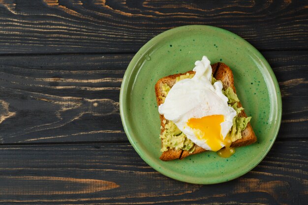 Toast und poschiertes Ei mit Avocado auf einer grünen Platte auf Holztisch