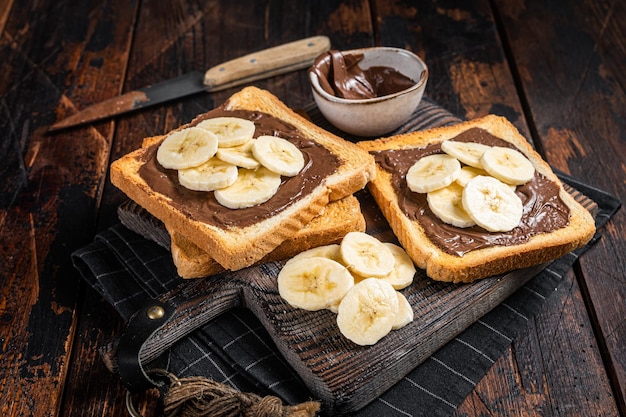 Toastbrot mit Bananen und Schokoladencreme auf Holzbrett Holzhintergrund Ansicht von oben