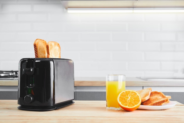 Toaster mit Geschirr und Toast mit frischem Saft auf einem hölzernen Küchentisch