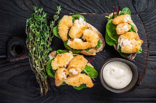 Toasts mit knusprig gebratenen Shrimps Garnelen und grünem Salat auf einem Holzbrett