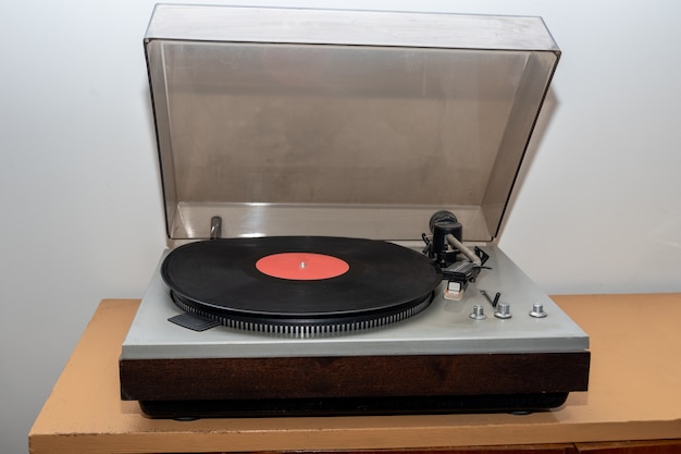 Toca-discos estéreo vintage retrô analógico em uma mesa de madeira. uma plataforma giratória de plástico antiquada tocando uma faixa de música, vista frontal. conceito de música retro