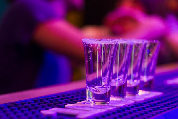 Foto toca de tequila en la mesa del bar por la noche gente de la fiesta en el fondo