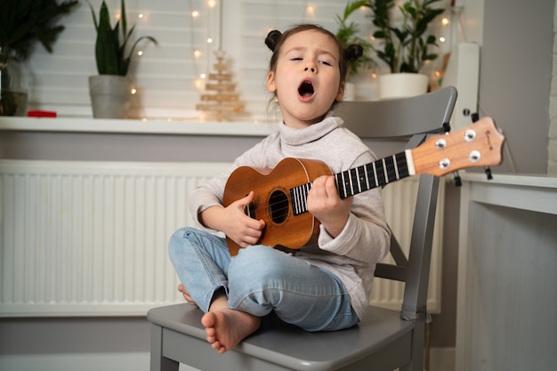 Toca el ukelele y canta. El desarrollo de la primera infancia. La niña tiene talento musical. Hermosa niña practicando canto y tocando la guitarra.