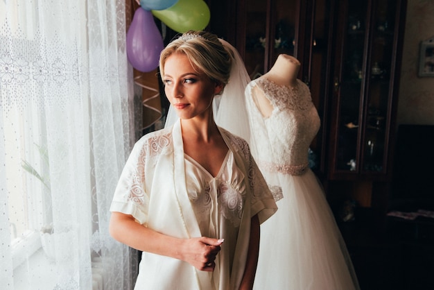 Tocador de la novia. Encantadora novia por la mañana en una bata se prepara para la celebración