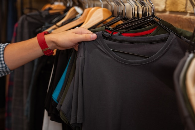 Tocando la camiseta. Comprador joven cuidadoso que visita la tienda de ropa de moda y toca una hermosa camiseta gris antes de comprarla