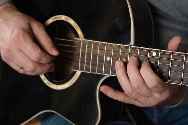 Tocando la guitarra Rasgueando la guitarra acústica Músico toca música Hombre dedos sosteniendo mediador Mano de hombre tocando el cuello de la guitarra en una habitación oscura Persona irreconocible ensayando el primer plano del diapasón