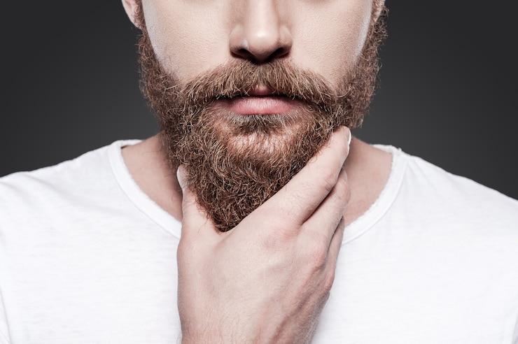 Foto tocando sua barba perfeita. close de um jovem barbudo tocando sua barba em pé contra um fundo cinza