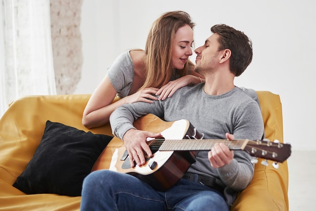 Tocando violão para a namorada na sala de estar da casa nova.