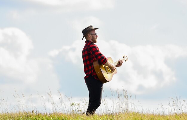 Tocar bela melodia Homem bonito com guitarra Estilo country Férias de verão Conceito de música country Guitarrista cantor country fica no fundo do céu de campo Músico country inspirado Canção de caminhada