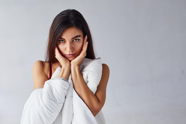 Tocar la cara con las manos. Mujer que cubre su cuerpo con una toalla en el estudio sobre fondo blanco.