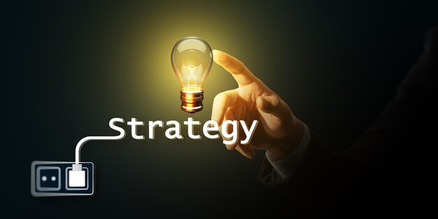 Tocar con la mano una bombilla incandescente con texto de estrategia que muestra el concepto de negocio y la innovación sobre un fondo oscuro