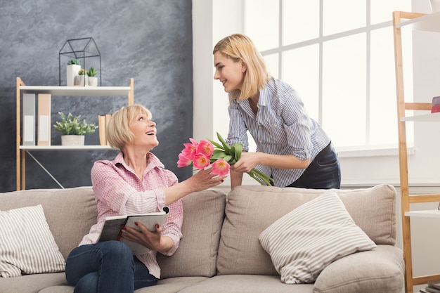 Tochter, die der erwachsenen Mutter Blumen schenkt. Gemeinsam Zeit verbringen, am Wochenende einen Urlaub zu Hause feiern. Generation, Beziehung, Überraschung und Muttertagskonzept