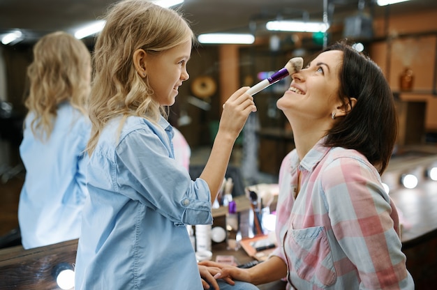 Tochter, die ihrer Mutter im Salon Make-up macht