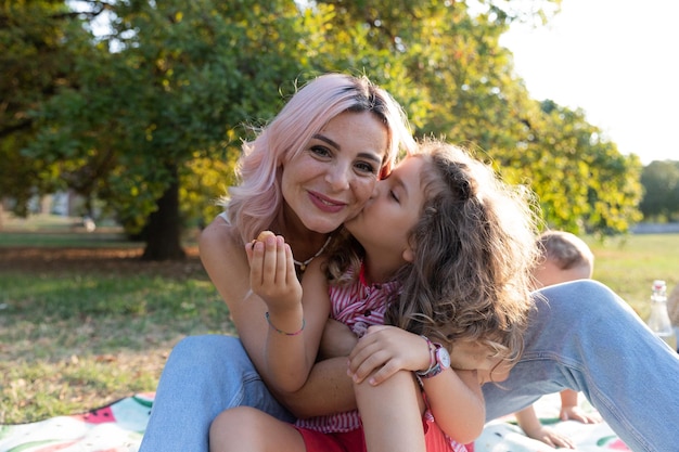 Tochter gibt ihrer Mutter während einer Picknick-Liebe zwischen Mutter und Tochter einen Kuss