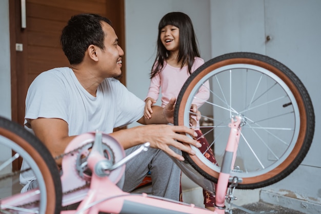 Tochter lacht glücklich, als ihr Vater sein kleines Fahrrad repariert