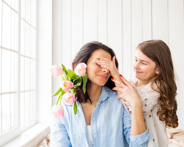 Tochter mit Blumen, die Augen der Mutter bedecken