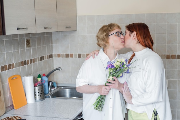 Tochter schenkt ihrer erwachsenen Mutter Blumen und küsst sie in der Küche. Am Wochenende feiert sie gemeinsam zu Hause den Muttertag